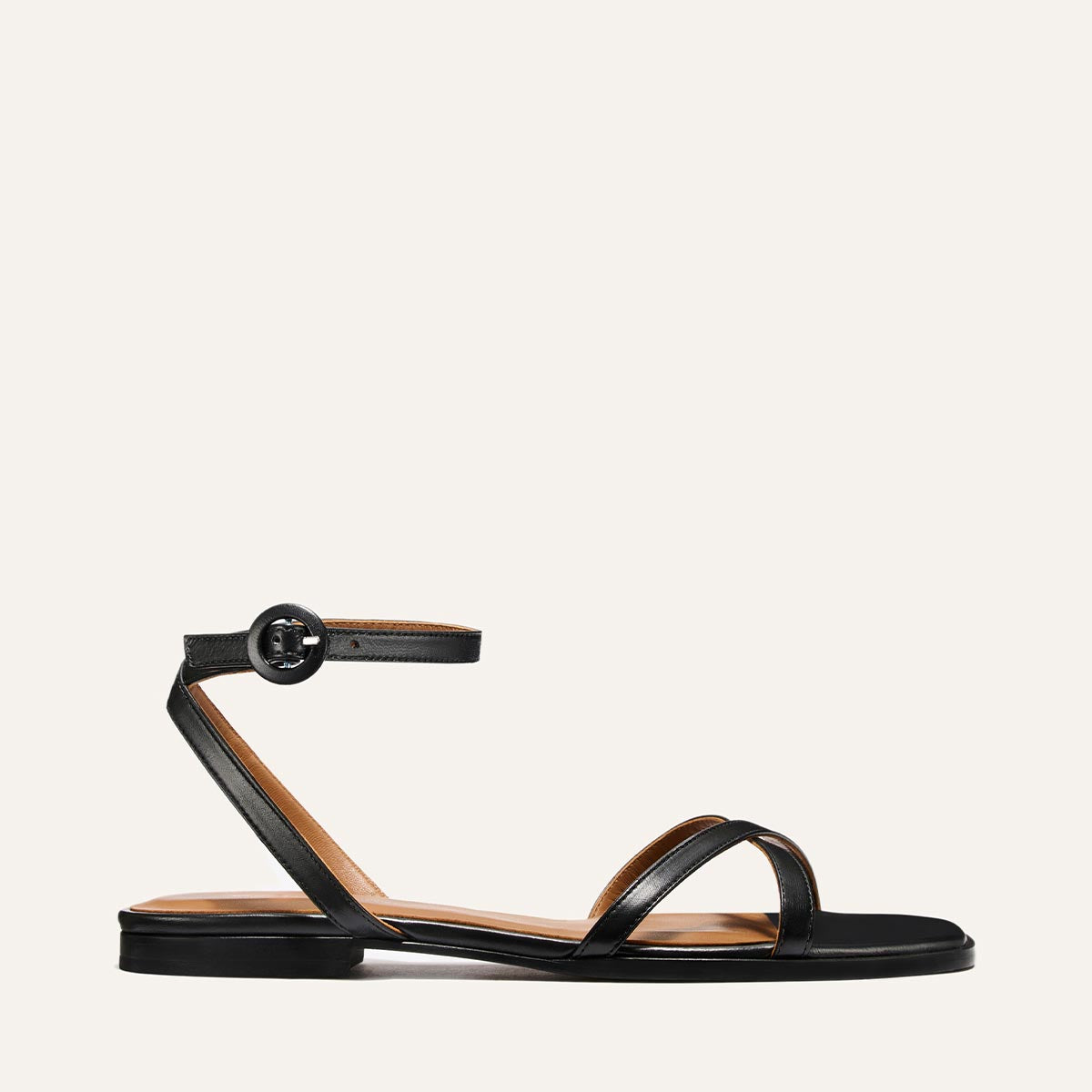The Flat Sandal - Black Nappa by Margaux features a minimalist black design with a thin ankle strap, buckle, and toe strap—perfect for those who love timeless style.