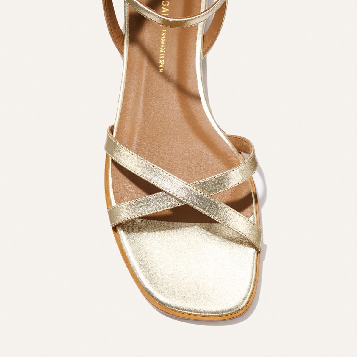 A close-up top view of Margaux’s The Flat Sandal - Champagne, featuring a square toe, two slim crisscrossing straps, and a foam-cushioned insole, set against a light background.