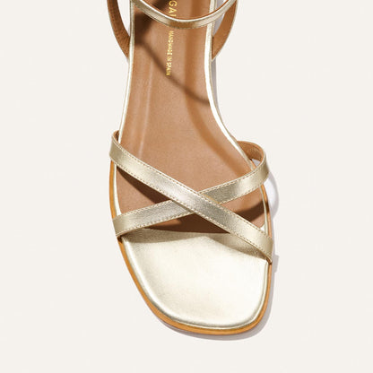A close-up top view of Margaux’s The Flat Sandal - Champagne, featuring a square toe, two slim crisscrossing straps, and a foam-cushioned insole, set against a light background.