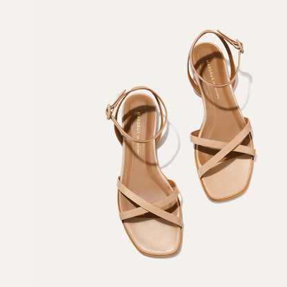 The Flat Sandal - Dune Nappa by Margaux: beige open-toe sandals with ankle straps and crisscross front bands, featuring a foam-cushioned insole for all-day comfort, shown on a light background.