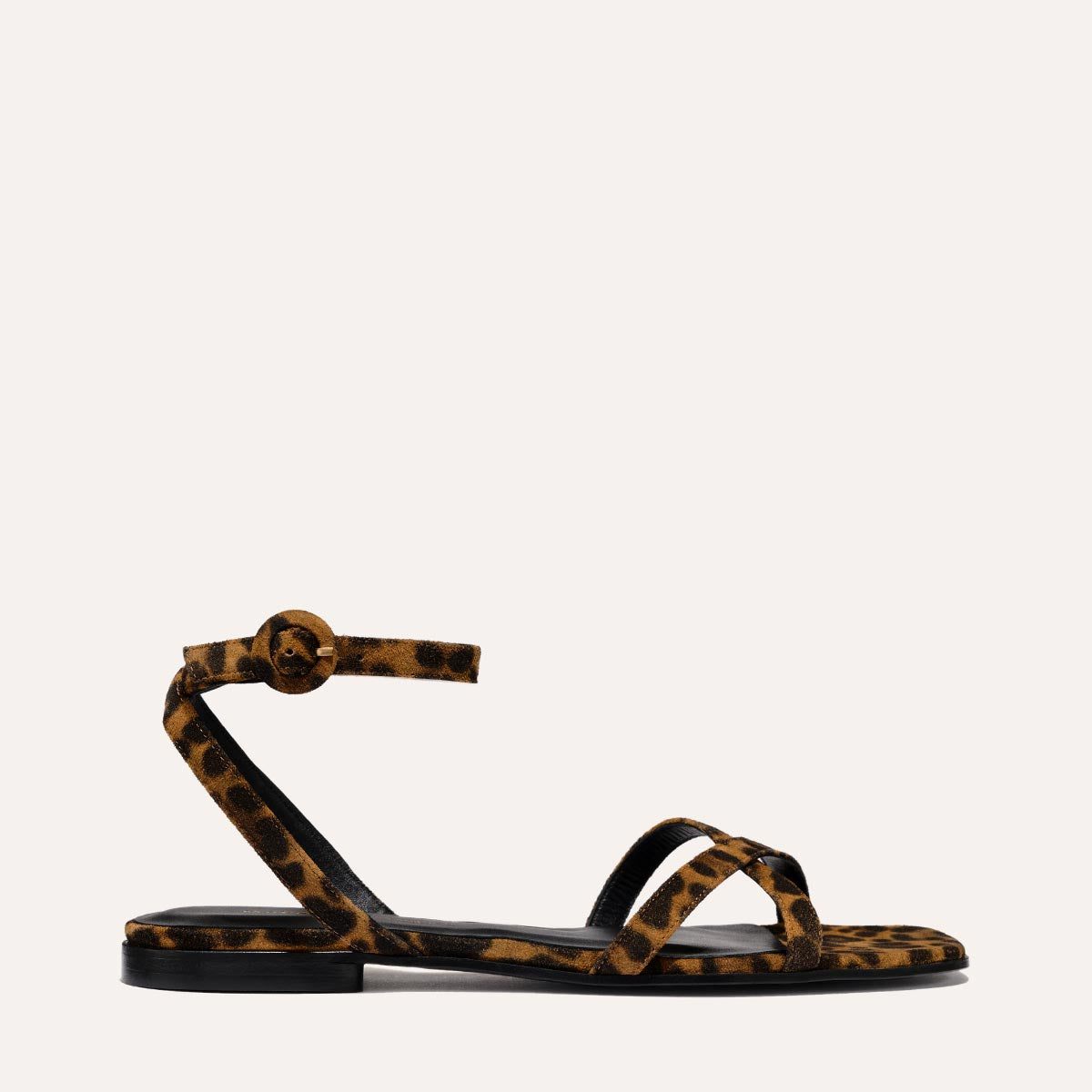 The Flat Sandal - Leopard Suede by Margaux is a handcrafted flat sandal in leopard-print suede, featuring a thin buckled ankle strap and two slim toe straps, shown on a plain light background.