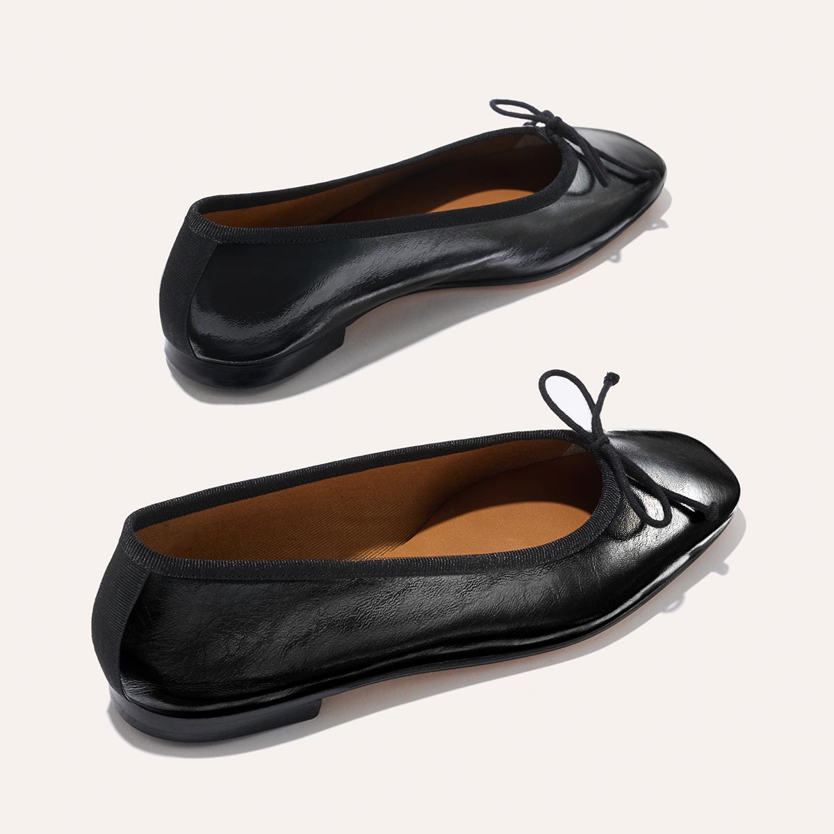 The Fonteyn by Margaux features black crinkle-gloss nappa leather ballet flats with rounded toes, delicate front bows, and low heels, shown on a light background.