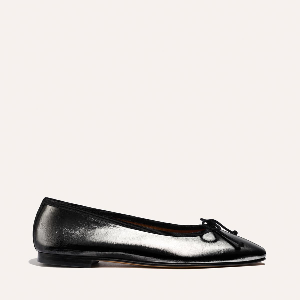 The Fonteyn by Margaux in Black Crinkle-Gloss Nappa is a ballet flat featuring a rounded toe, low heel, and small bow detail, shown against a plain light background.