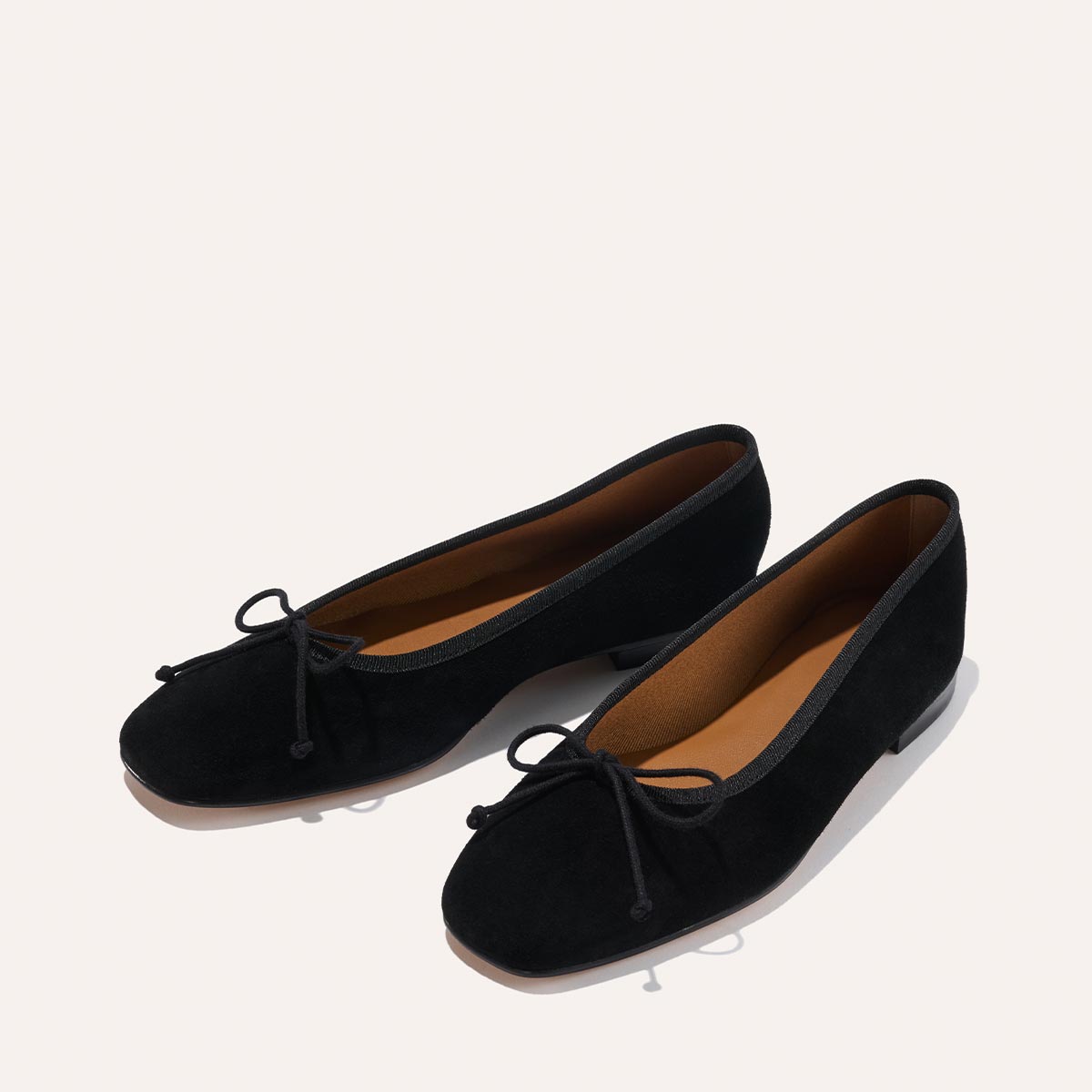 The Fonteyn - Black Suede by Margaux features classic black suede ballet flats with rounded toes, low heels, and bow accents, handcrafted for comfort and shown on a light background.