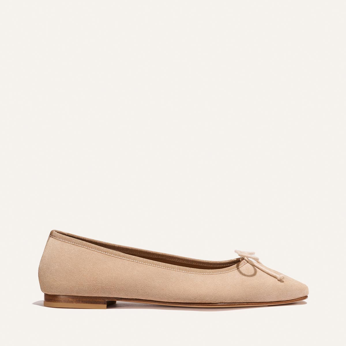 The Fonteyn - Cameo Suede by Margaux features a beige suede ballet flat with a small bow on the rounded toe, a low wooden heel, and minimal detailing, shown against a plain white background.