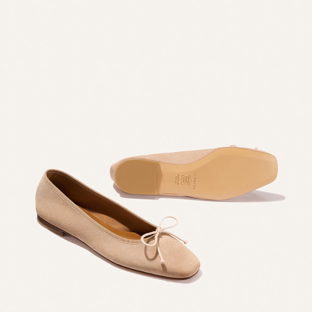 The Fonteyn - Cameo Suede ballet flats by Margaux are shown on a white background: one upright, the other displaying the sole. The beige suede shoes feature a small bow on the front.