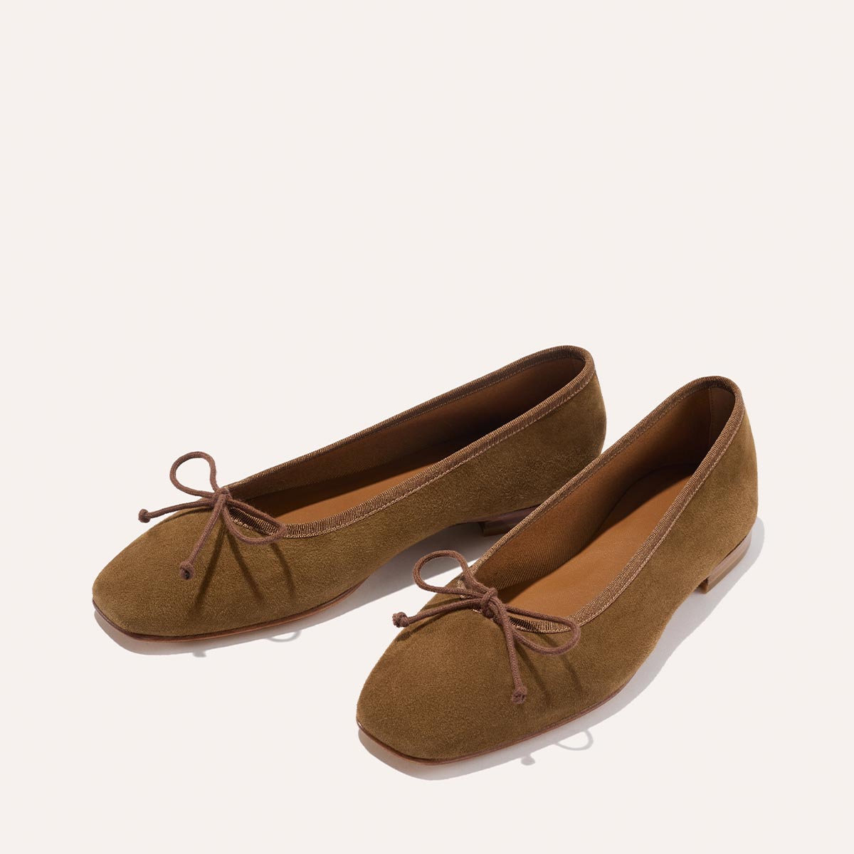 The Fonteyn - Cedar Suede by Margaux: brown suede ballet flats with rounded toes, low heels, and matching brown bow accents on the front, displayed on a light background.