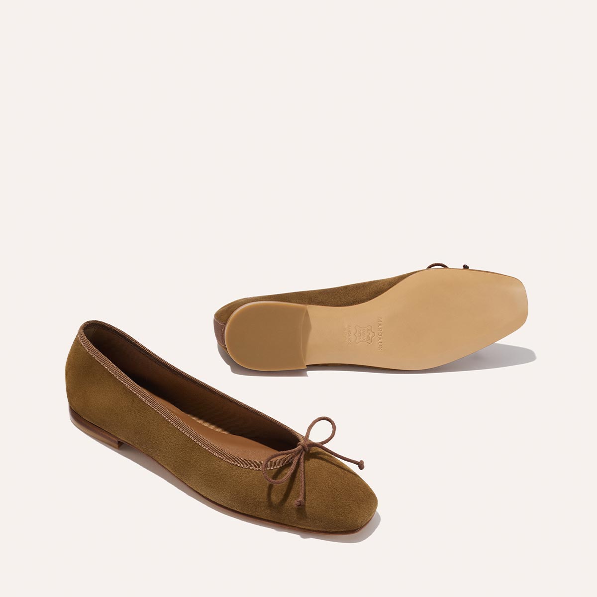 The Fonteyn - Cedar Suede by Margaux: a pair of brown suede ballet flats with a delicate bow and flat rubber soles, shown on a light background—one upright, one on its side to display the sole.