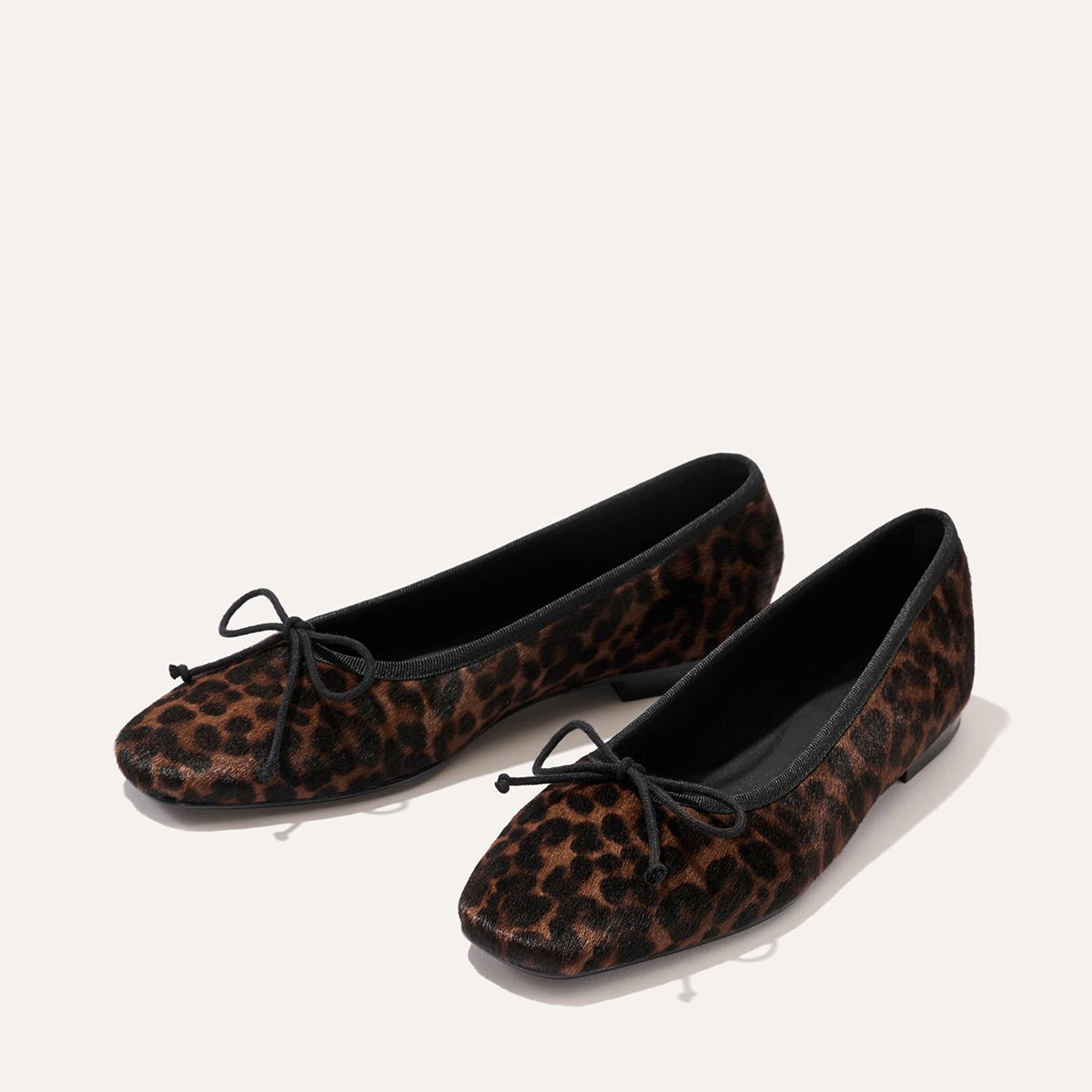 A pair of Margaux’s The Fonteyn - Chocolate Leopard Haircalf ballet flats, featuring handcrafted leopard print, black trim, and black bow accents, designed for all-day comfort and showcased on a light background.