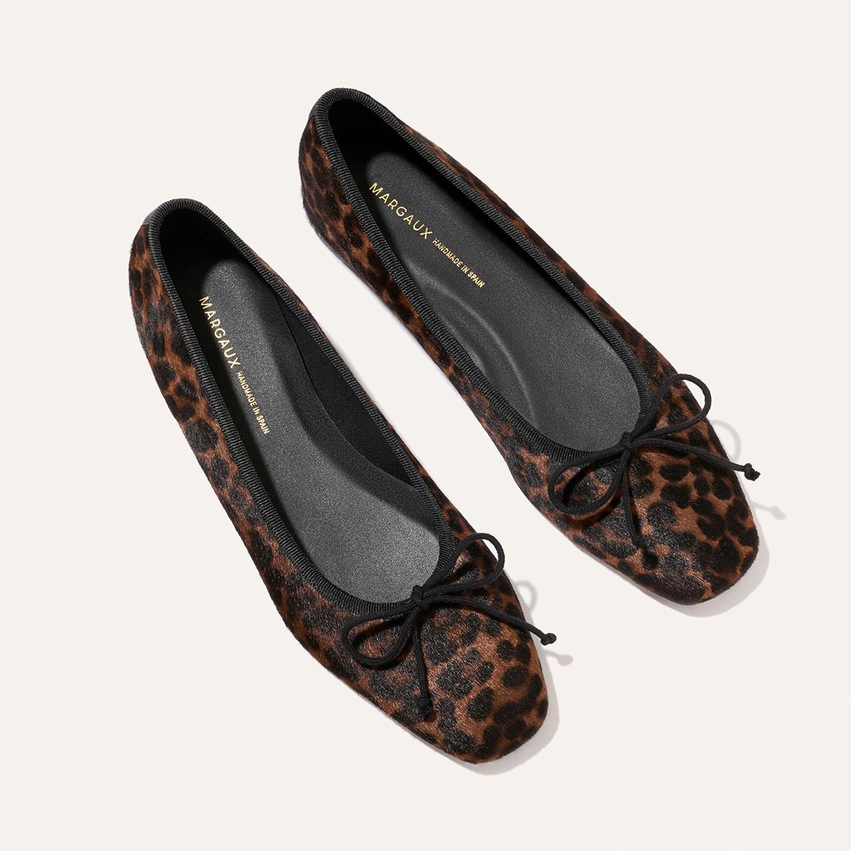 A pair of Margaux’s The Fonteyn ballet flats in chocolate leopard haircalf, featuring black trim, a black bow at the toe, and a black interior lining.