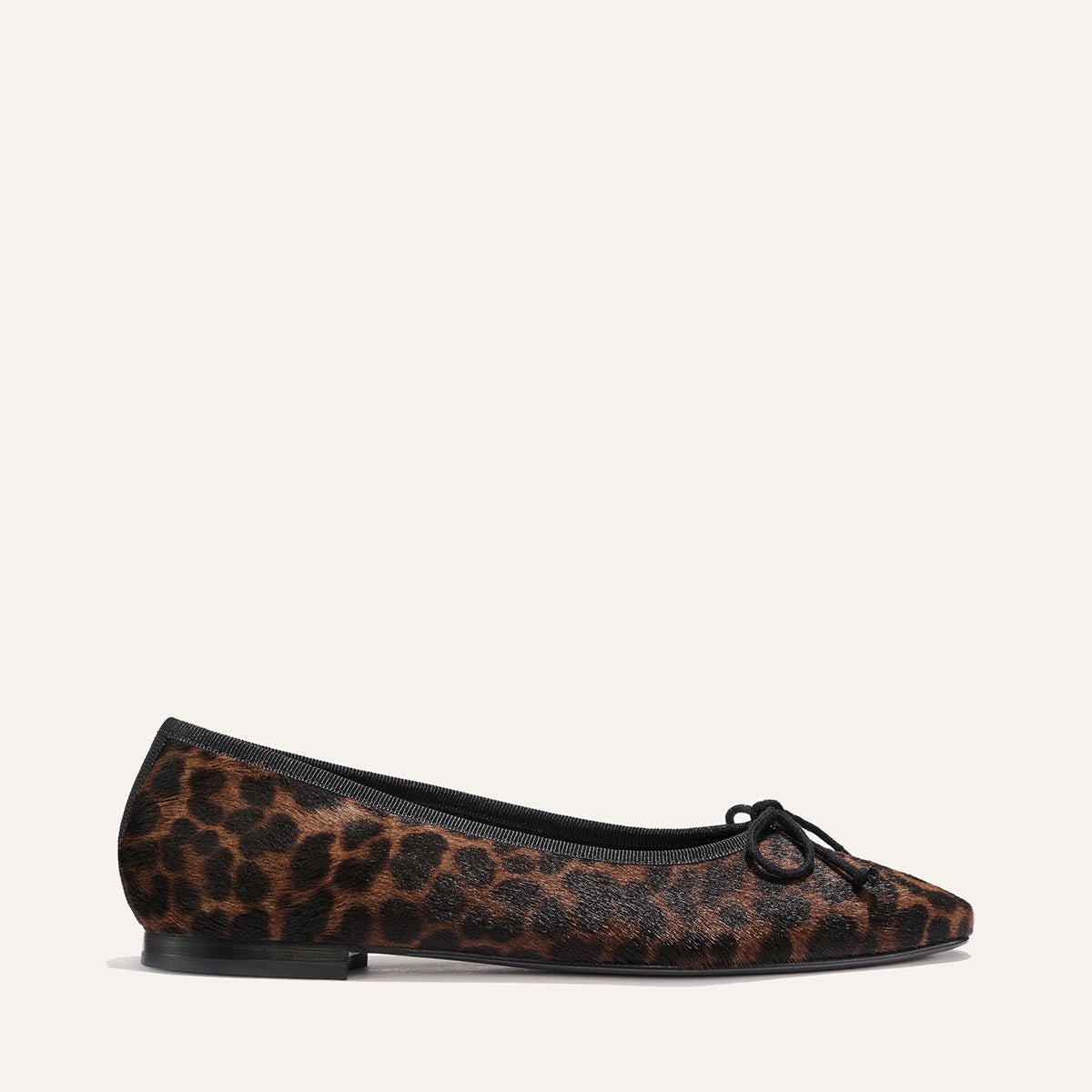 Here’s a rewritten sentence using the provided product data: The Fonteyn - Chocolate Leopard Haircalf ballet flat by Margaux, handcrafted with a black bow on the toe, black trim around the opening, and a flat black sole, is shown individually against a plain light background.