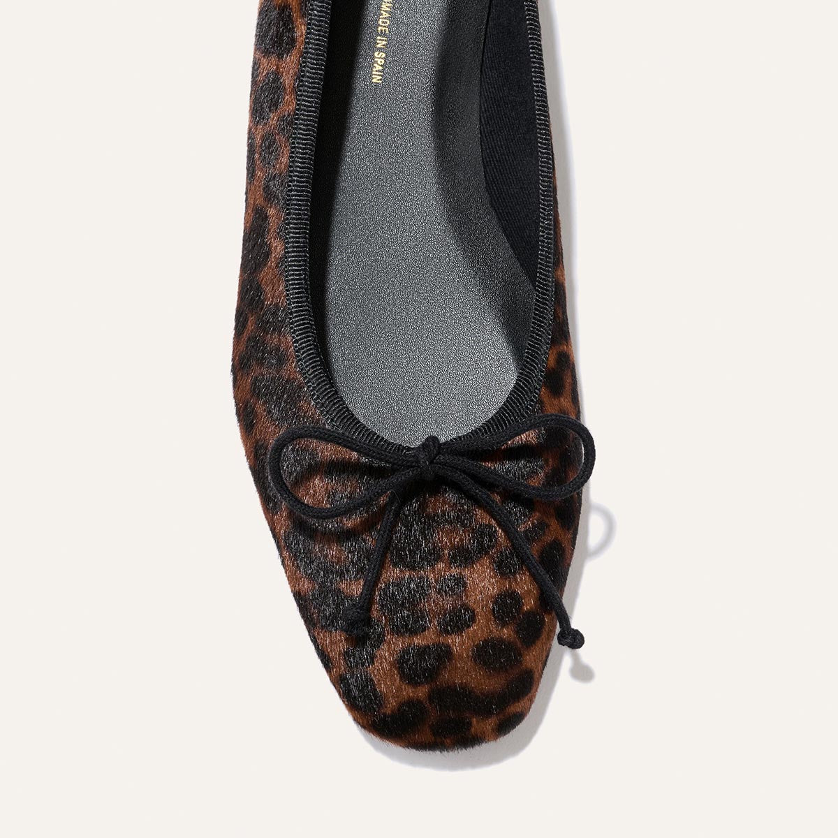 A close-up of Margaux’s The Fonteyn in Chocolate Leopard Haircalf, a single handcrafted ballet flat featuring a small black bow on the toe, photographed from above on a light background to showcase its comfort-first design.