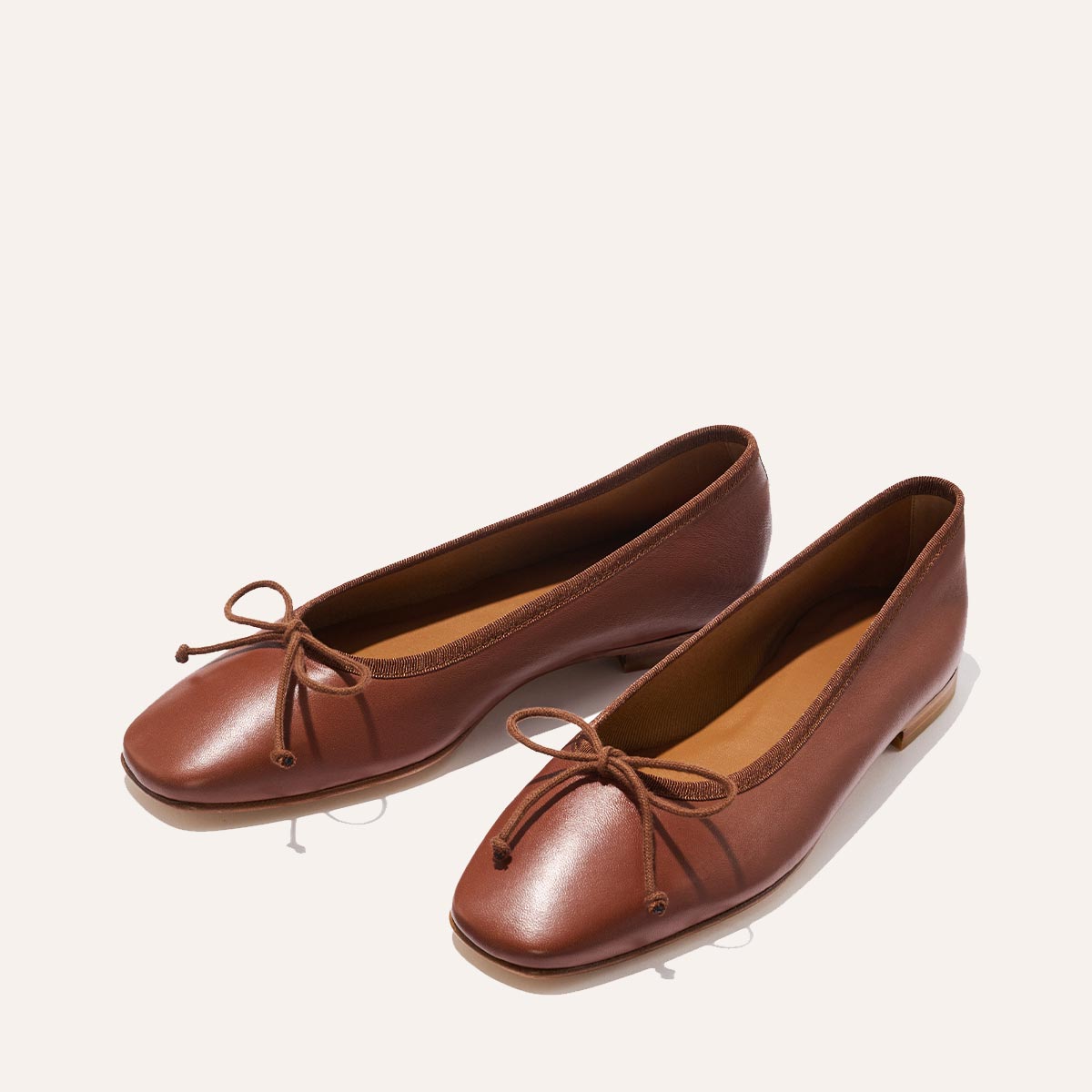 The Fonteyn - Cognac Nappa by Margaux: brown leather ballet flats with rounded square toes and small front bows, shown on a light beige background.