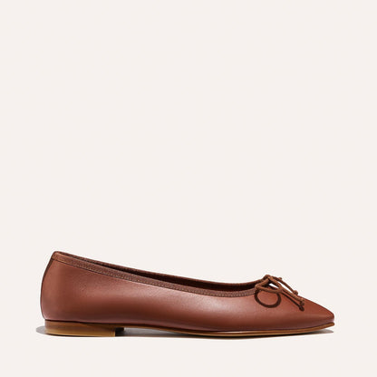 The Fonteyn - Cognac Nappa by Margaux: a brown leather ballet flat with a small bow on the rounded toe, shown in side view against a plain light background.