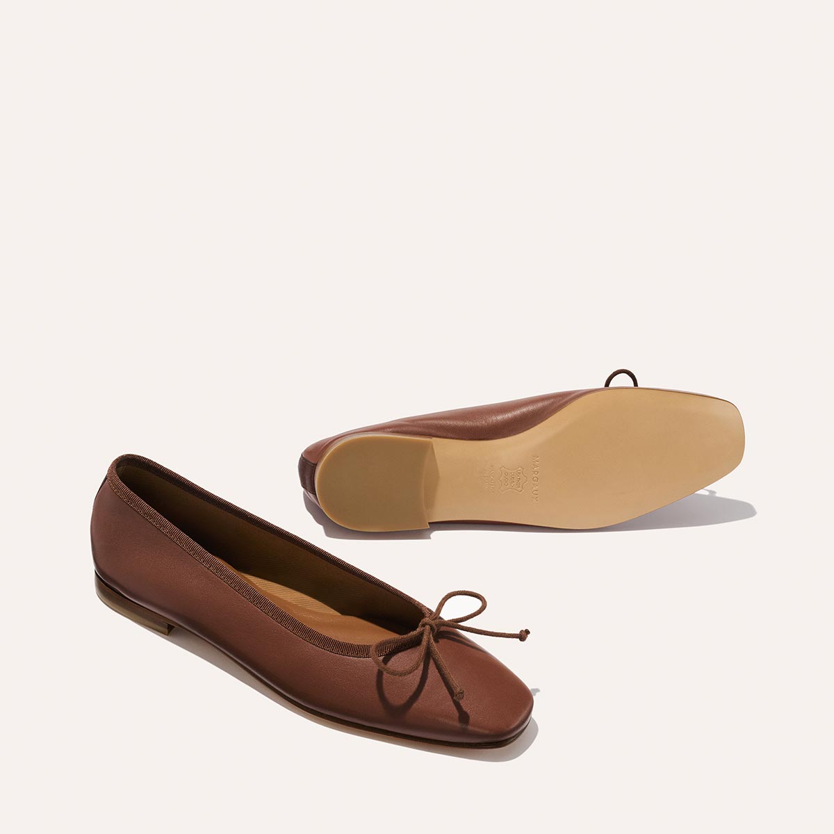 Two brown leather The Fonteyn - Cognac Nappa ballet flats, one showing the chic squared-off toe and bow detail, the other showing the sole.