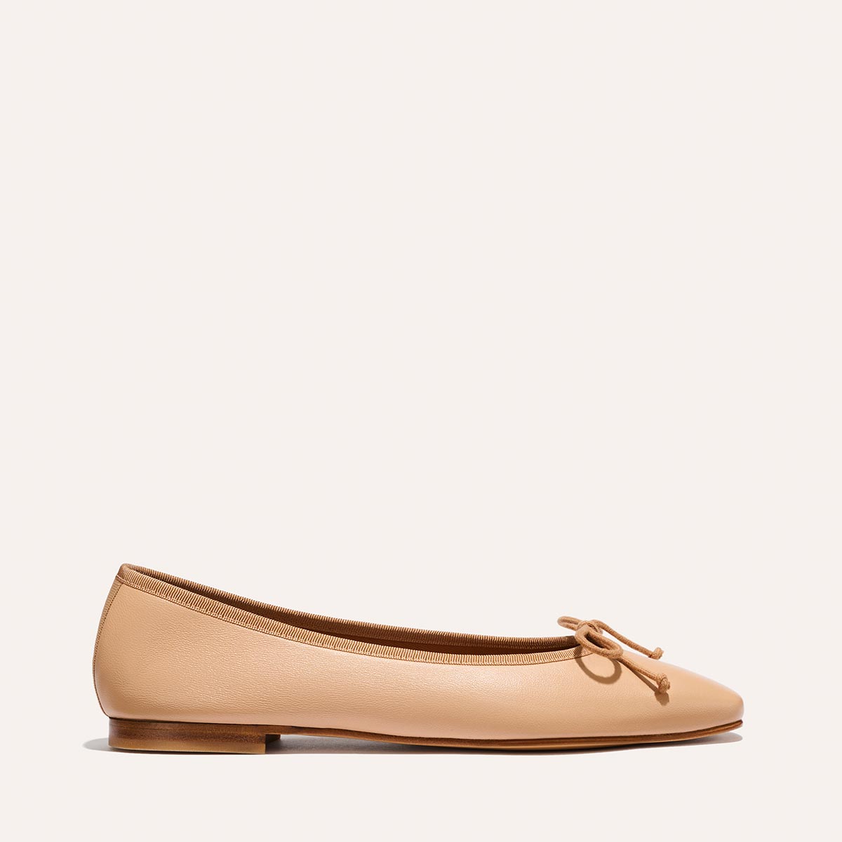 The Fonteyn - Dune Nappa by Margaux is a tan ballet flat featuring a small bow, low heel, and minimalist design, shown against a plain light background.
