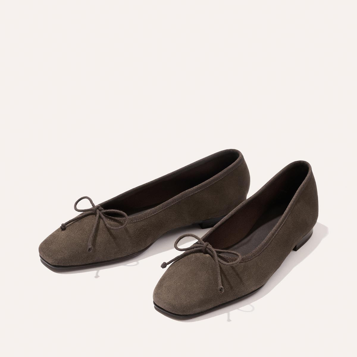 A pair of handcrafted olive green suede ballet flats with square toes and decorative bows on top, displayed on a light background.