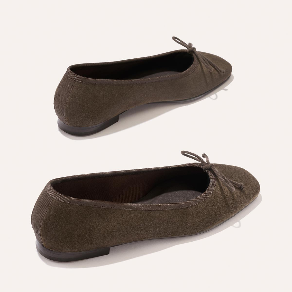 A pair of The Fonteyn ballet flats by Margaux in English Brown Suede, featuring small bows on the front and displayed from slightly different angles against a plain light background.
