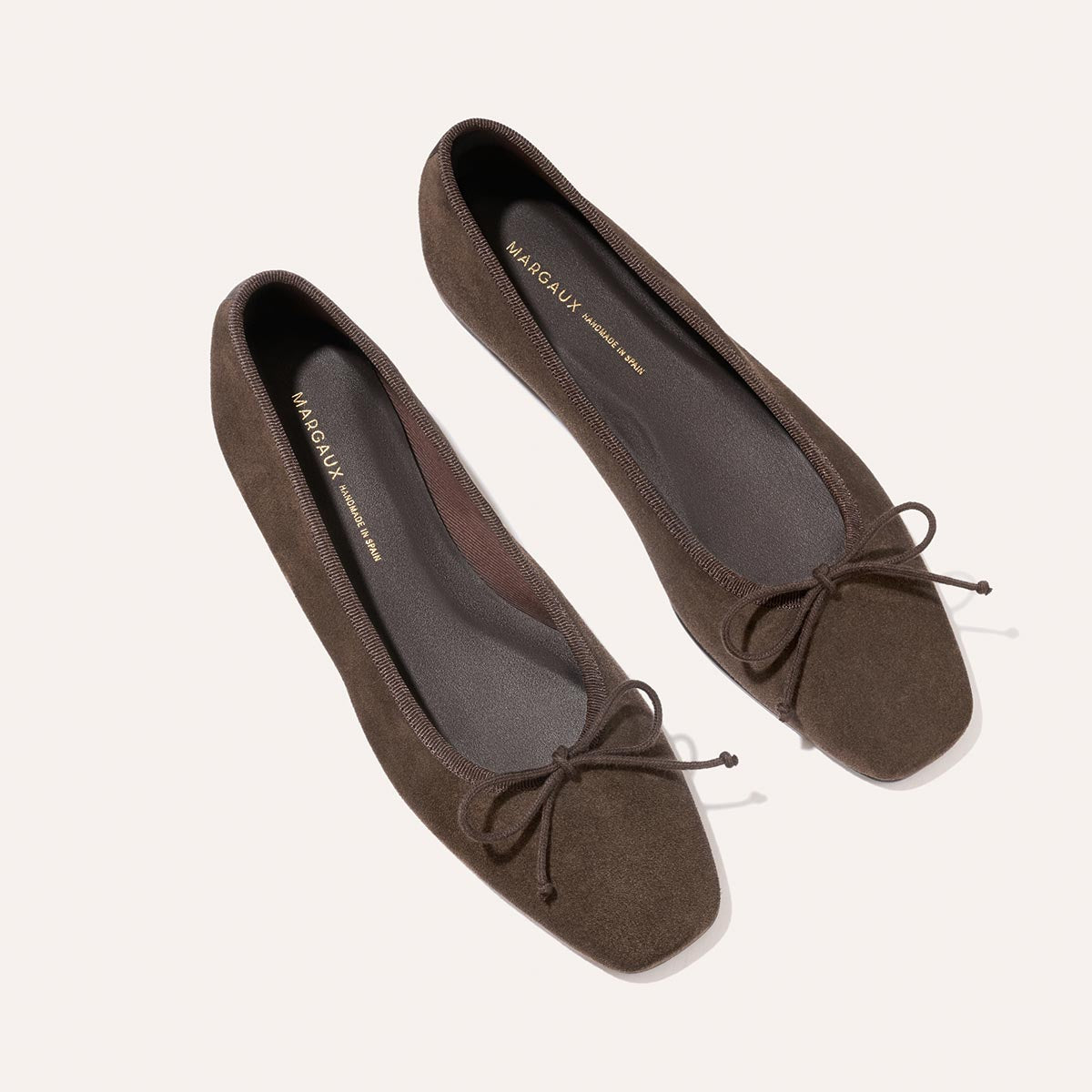 A pair of “The Fonteyn” ballet flats by Margaux in English Brown Suede, featuring square toes and delicate bows, handcrafted for comfort and shown from above on a light background.