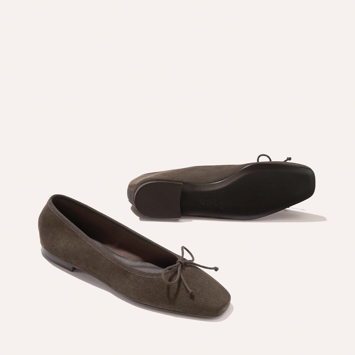 A pair of The Fonteyn - English Brown Suede ballet flats with a chic bow on the toe, shown from the side and the comfort-first sole.