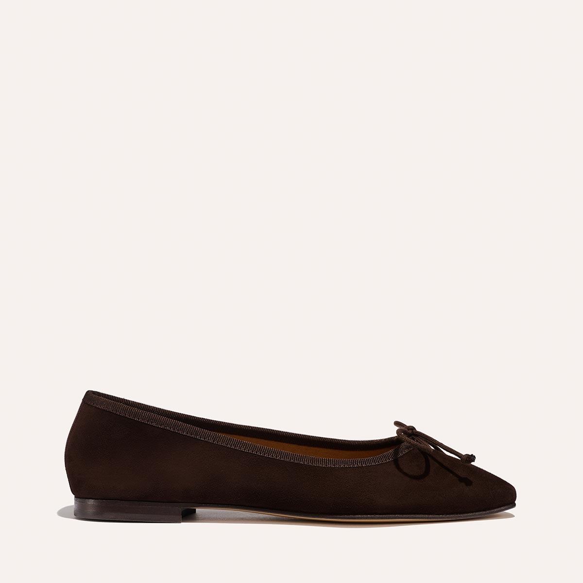 The Fonteyn - Espresso Suede by Margaux is a dark brown handcrafted ballet flat with a round toe, delicate front bow, and thin black sole, shown on a light background.