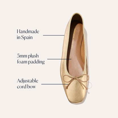 The Fonteyn - Gold Crinkle Nappa by Margaux is a gold ballet flat with a squared-off toe, handmade in Spain. It features 5mm plush foam padding, an adjustable cord bow, and a soft tan interior for signature comfort.