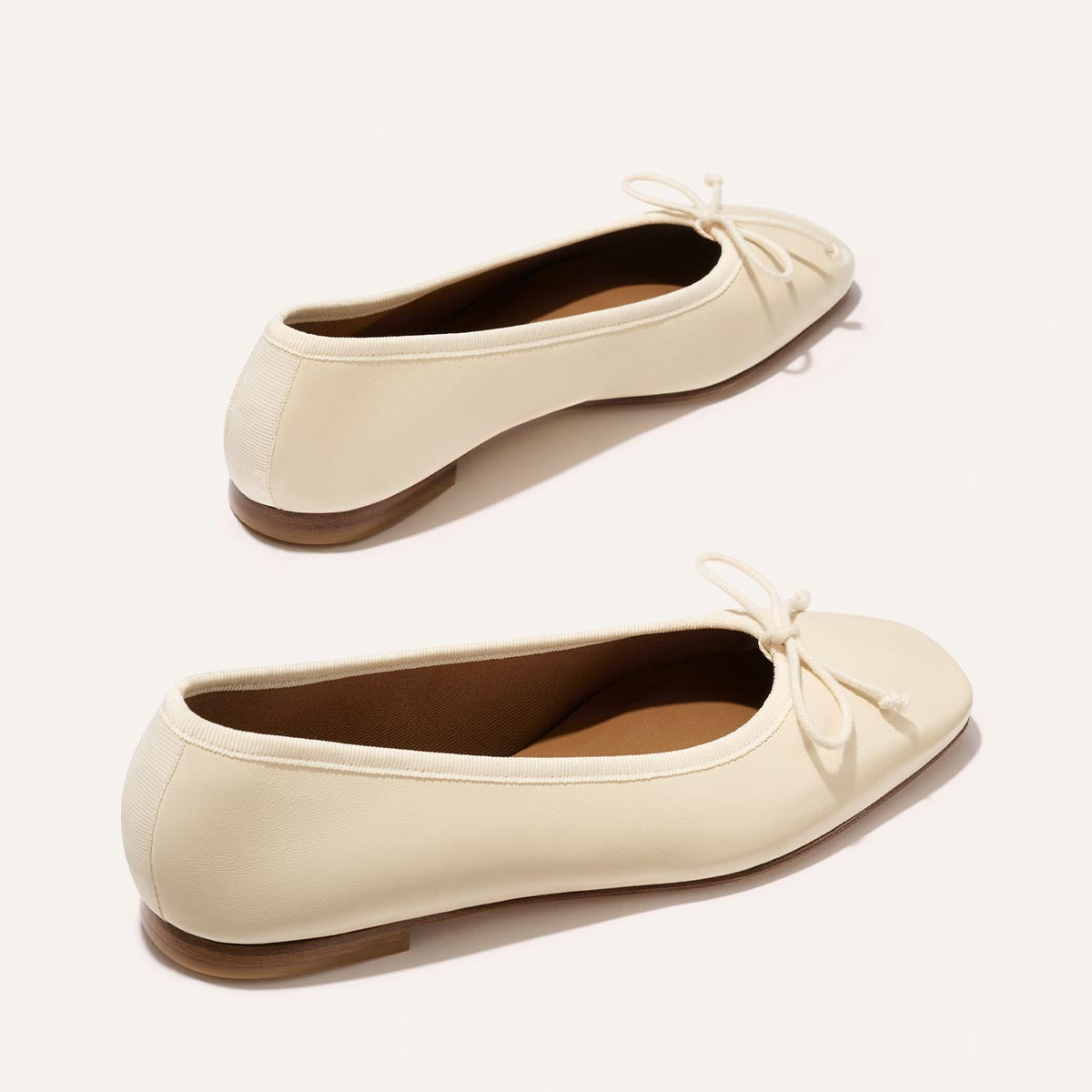 Pair of cream-colored flats with a bow detail on a white background