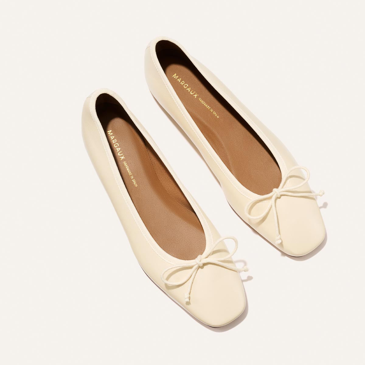 Pair of cream-colored flats with a bow detail on a white background