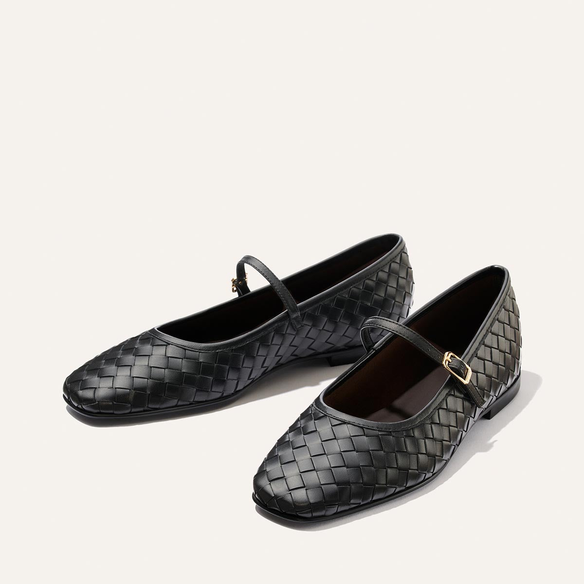 A pair of The Fonteyn Jane flats by Margaux, crafted in black woven Pasado Nappa leather with gold buckles, displayed on a light background.
