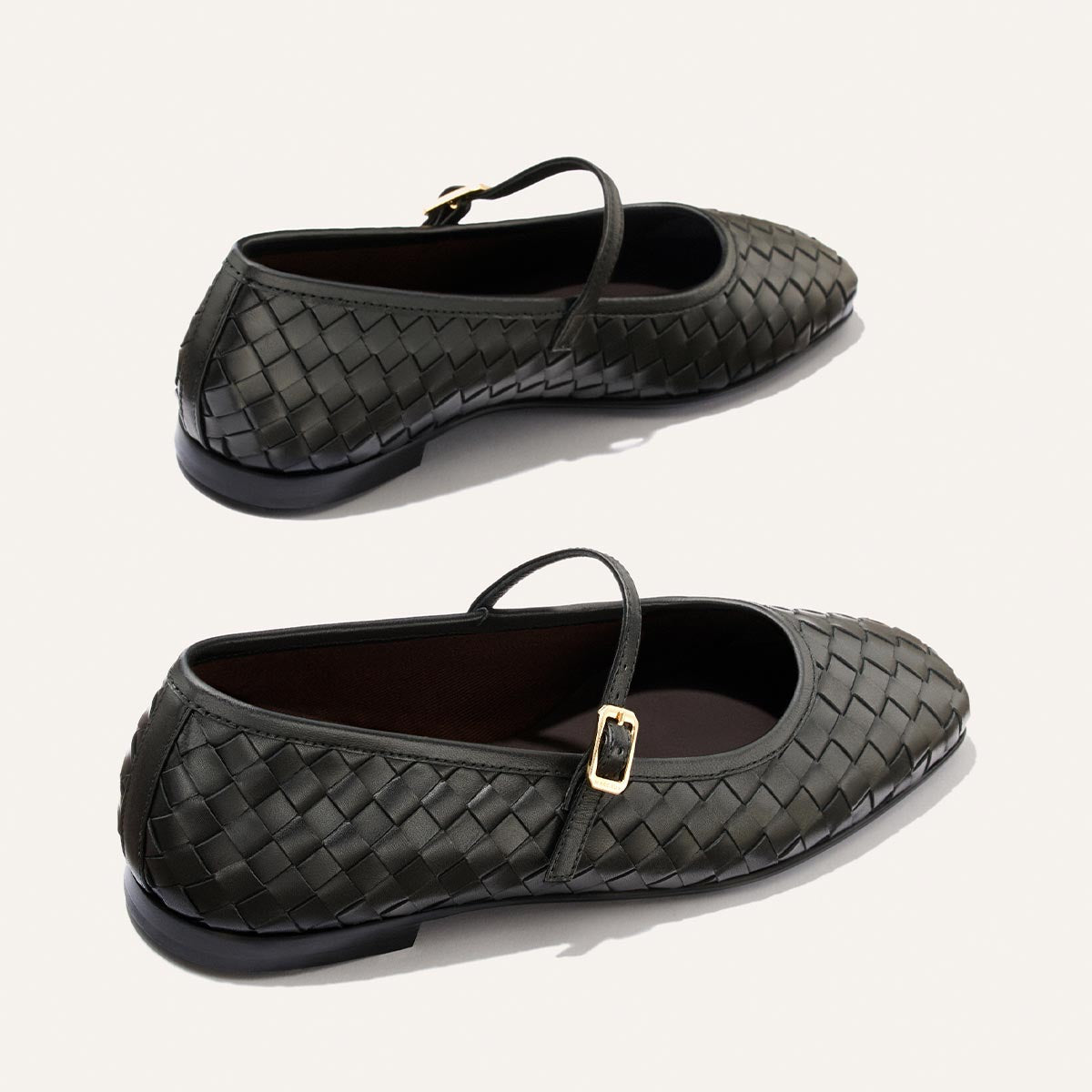 Two Margaux "The Fonteyn Jane" flats in black woven Pasado Nappa leather, featuring Mary Jane straps with gold buckles and black soles, displayed on a light background.