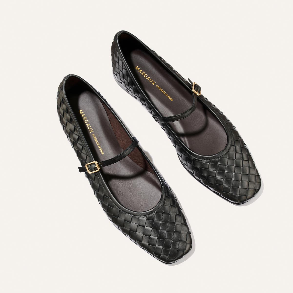 A pair of The Fonteyn Jane flats by Margaux, crafted in black woven Pasado Nappa leather with gold buckles, displayed on a light background.