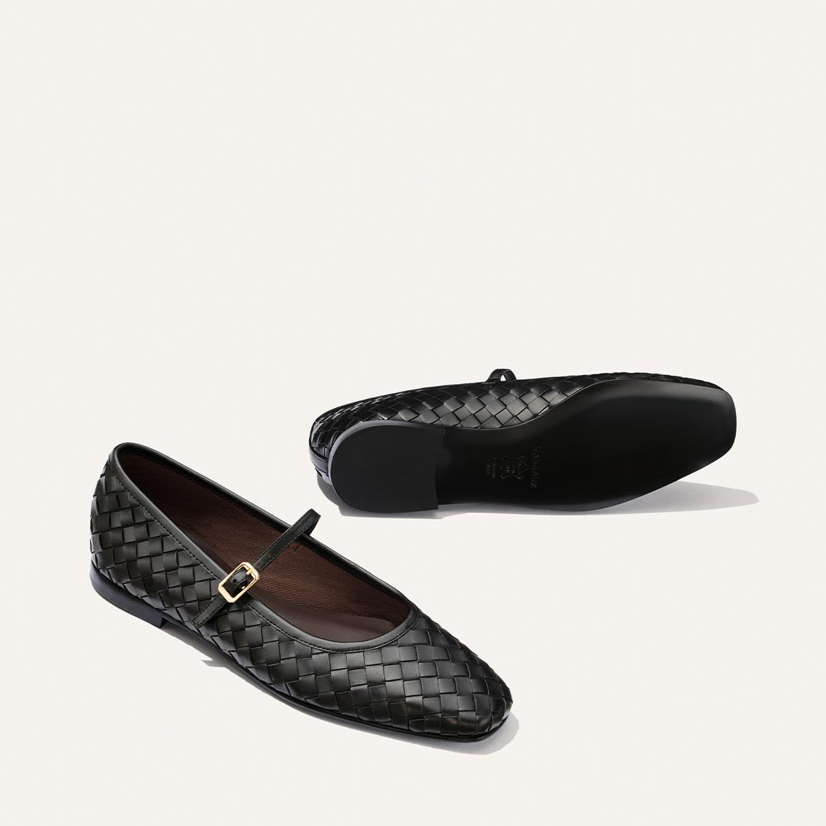 Two Margaux "The Fonteyn Jane" flats in Black Woven Pasado Nappa are displayed on a white background; one is upright, highlighting the side profile and gold buckle, while the other lies flat with the sole visible.