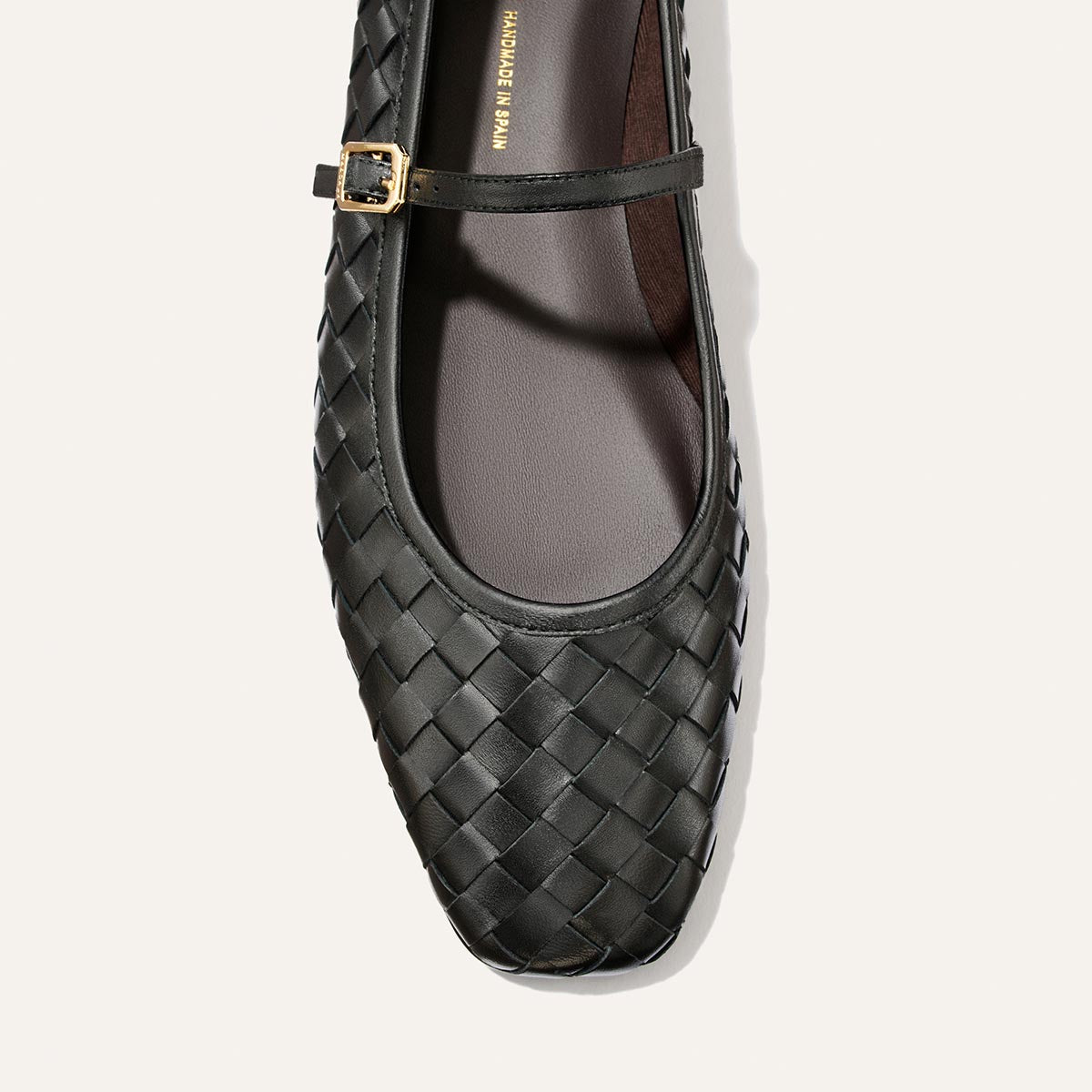 A top view of The Fonteyn Jane by Margaux in Black Woven Pasado Nappa leather, featuring a small gold buckle on the Mary Jane strap, displayed on a light background.
