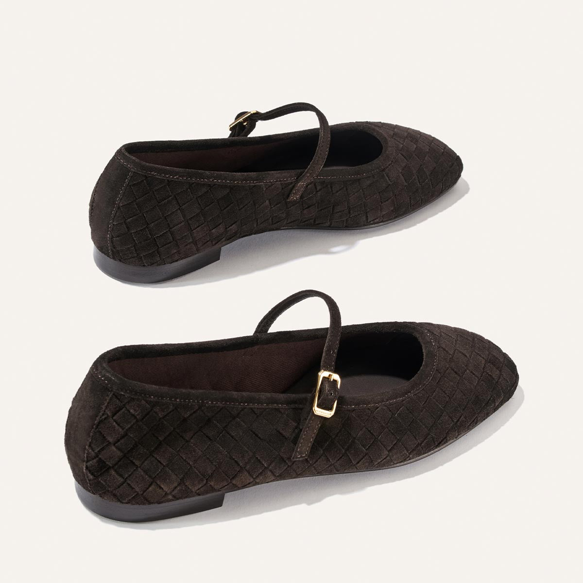 A pair of Margaux’s The Fonteyn Jane flats in dark chocolate woven Pasado suede, featuring gold buckles, displayed from side and three-quarter views against a plain white background.
