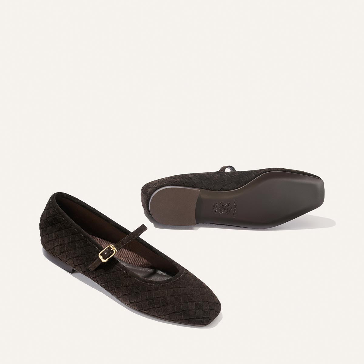 A pair of The Fonteyn Jane flats by Margaux in dark chocolate woven Pasado suede: one shoe faces left, displaying a gold buckle strap, while the other reveals the sole. Both are set against a plain off-white background.