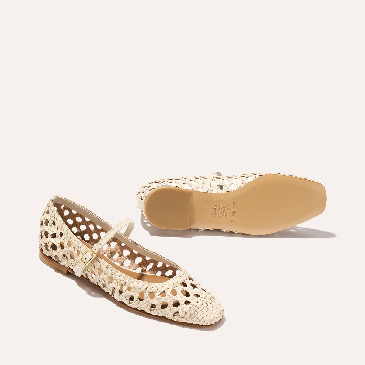 The Fonteyn Jane - Ecru Woven Leather flats by Margaux feature a handwoven cream finish and adjustable strap. One shoe is upright, showing the side and top, while the other reveals the sole against a plain, light background.