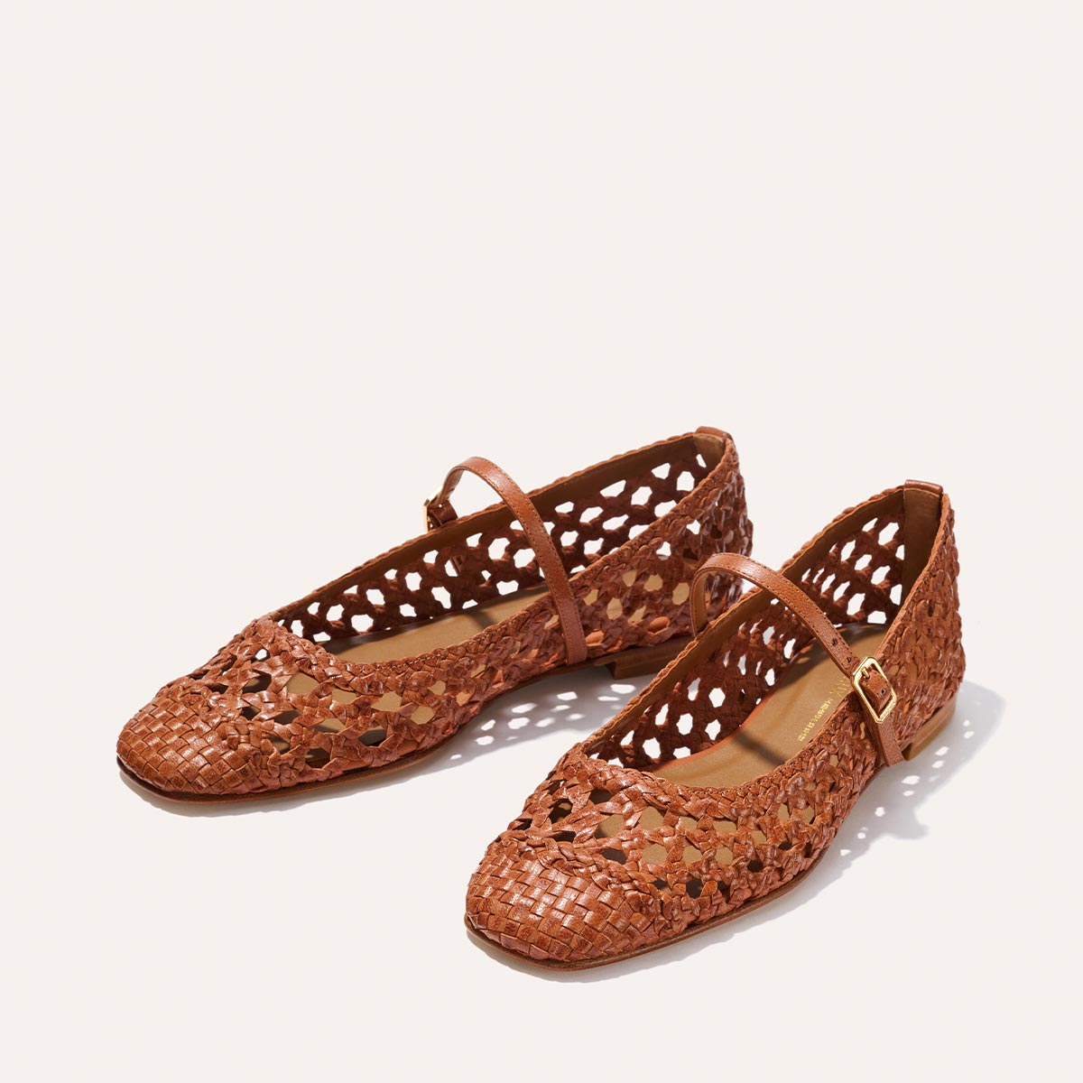 Margaux's The Fonteyn Jane - Saddle Woven Leather flats feature brown handwoven leather, perforated detailing, adjustable ankle straps, and gold buckles, shown on a light background.