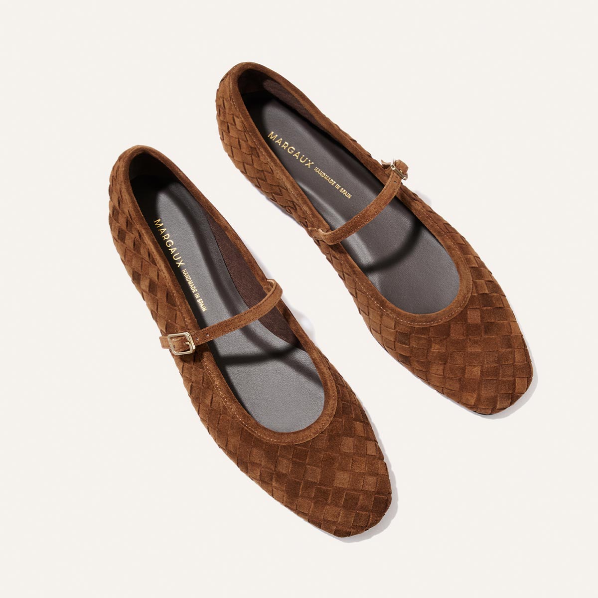 A pair of The Fonteyn Jane flats in Saddle Woven Pasado Suede by Margaux, displayed from above on a light background. Each shoe features a thin buckled strap and a dark interior with gold Margaux branding.