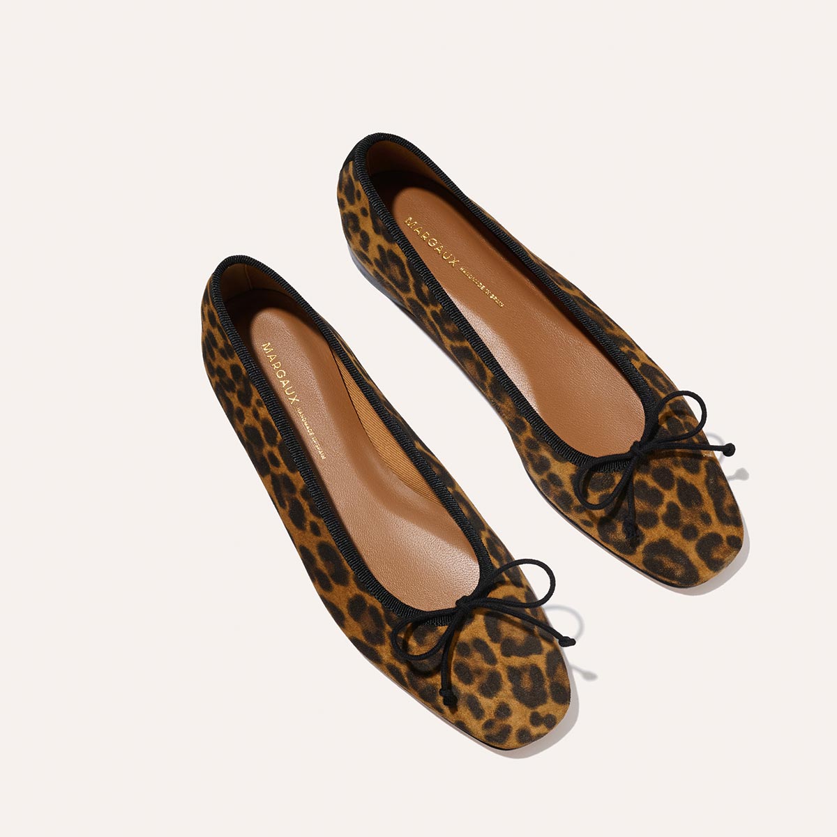 The Fonteyn - Leopard Suede by Margaux: leopard print ballet flats featuring black trim and small black bows on the toes, displayed on a light background.