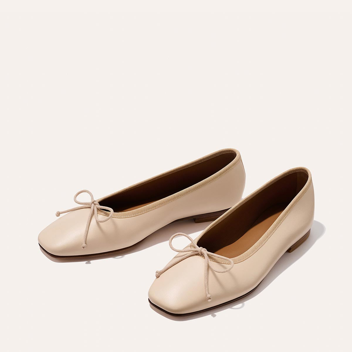 The Fonteyn - Magnolia Nappa by Margaux: handcrafted beige leather ballet flats with square toes and delicate bows, designed for comfort and shown on a light background.