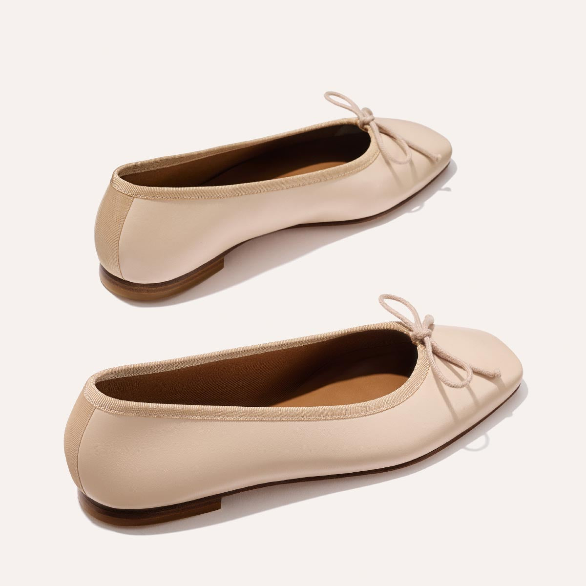 The Fonteyn - Magnolia Nappa by Margaux: comfort-first light beige ballet flats with small front bows, rounded toes, and flat brown soles, shown on a plain light background.