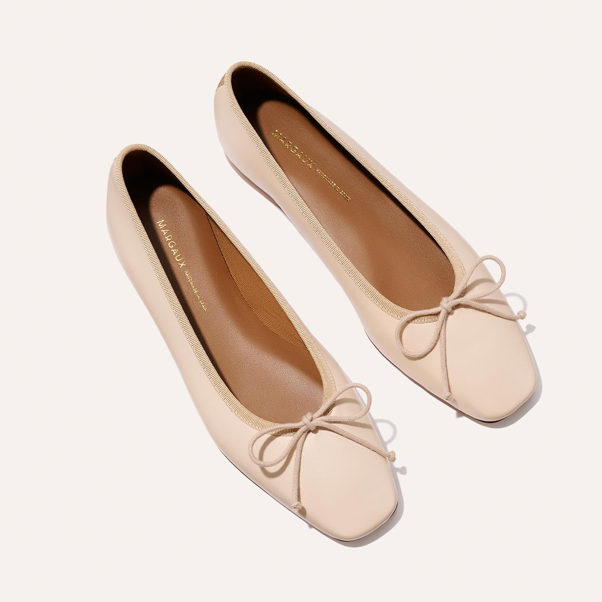 The Fonteyn - Magnolia Nappa by Margaux: handcrafted light beige ballet flats featuring square toes and delicate bows on the front, shown on a white background.