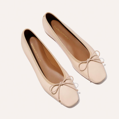 The Fonteyn - Magnolia Nappa by Margaux: handcrafted light beige ballet flats featuring square toes and delicate bows on the front, shown on a white background.