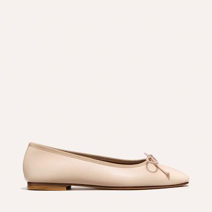 The Fonteyn - Magnolia Nappa by Margaux is a comfort-first beige ballet flat with a small bow on the rounded toe, a low wooden heel, and a smooth leather finish, shown on a plain light background.