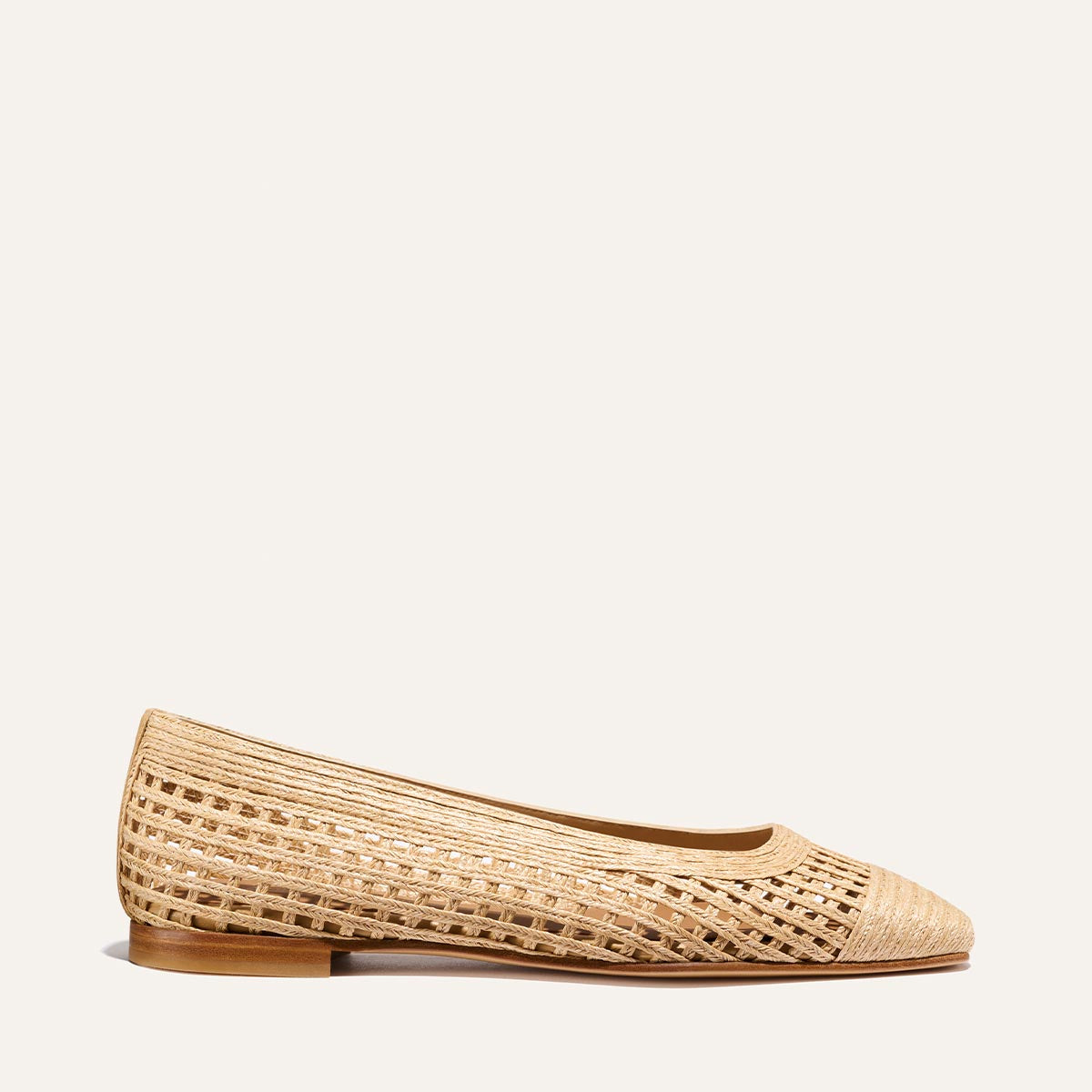 The Fonteyn - Natural Grid Raffia by Margaux is a tan woven flat with a pointed toe and low wooden heel, echoing Julia Berolzheimer’s elevated style, shown on a simple light background.