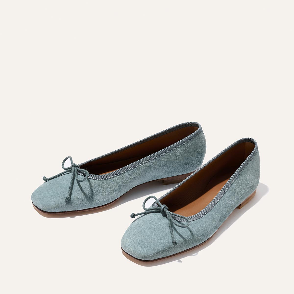 Margaux’s The Fonteyn - Ocean Suede: handcrafted light blue suede ballet flats with bows, brown soles, and rounded toes designed for comfort, shown on a plain white background.