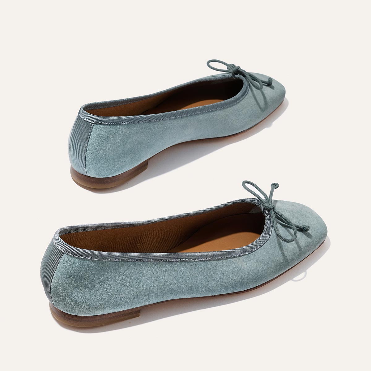 The Fonteyn - Ocean Suede by Margaux: light blue suede ballet flats with rounded toes, front bows, tan insoles, and flat brown soles—shown on a light background.
