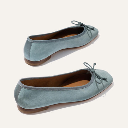 The Fonteyn - Ocean Suede by Margaux: light blue suede ballet flats with rounded toes, front bows, tan insoles, and flat brown soles—shown on a light background.