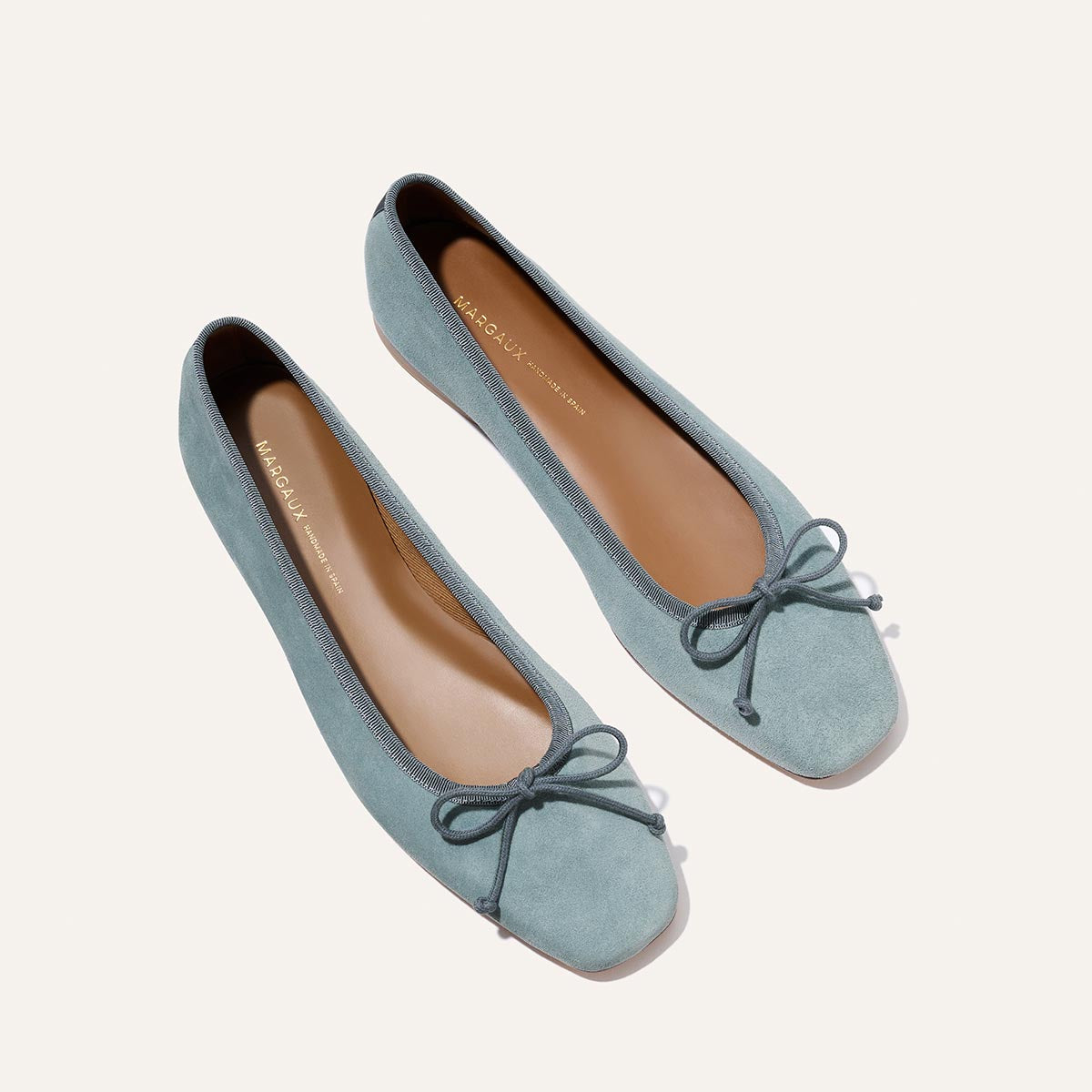 The Fonteyn - Ocean Suede by Margaux: handcrafted light blue suede ballet flats with rounded toes, matching bows, tan insoles, and light brown outsoles, displayed on a plain off-white background.