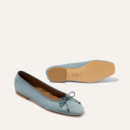 The Fonteyn - Ocean Suede by Margaux: light blue suede ballet flats with bow accents. One comfort-focused shoe stands upright; the other is sole-up, revealing its tan leather bottom.